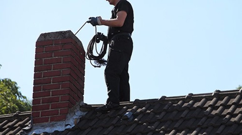 A chimney sweep at work atop a roof